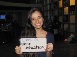 Student holding a sign that says “Love is peer education”